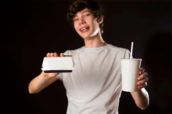 Samec číšník držet fast food soda box s hamburgery a papírové krabice potravin izolované na tmavém pozadí b — Stock fotografie