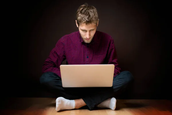Jovem homem sentar no chão e usar laptop no fundo escuro b — Fotografia de Stock