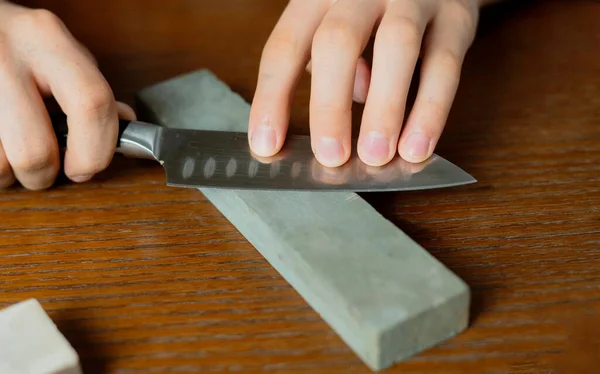 Jovem afiando uma faca na mesa de madeira no fundo escuro b — Fotografia de Stock