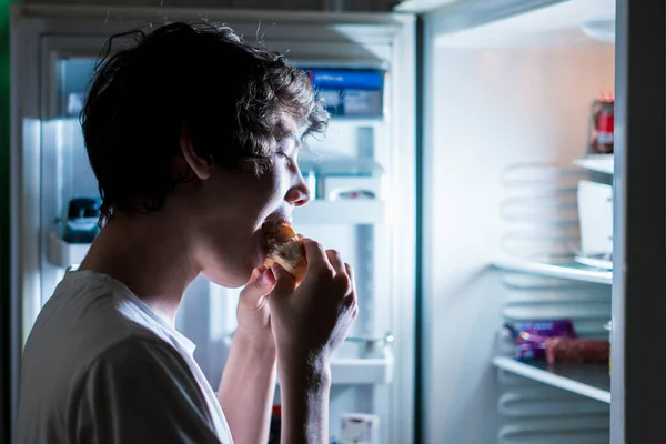 Nälkäinen henkilö syö roskaruokaa yöllä — kuvapankkivalokuva