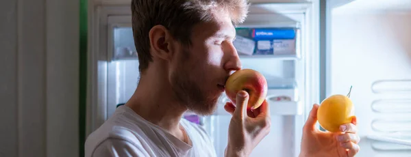 Henkilö syö terveellistä ruokaa hedelmiä jääkaapista myöhään yöllä f — kuvapankkivalokuva