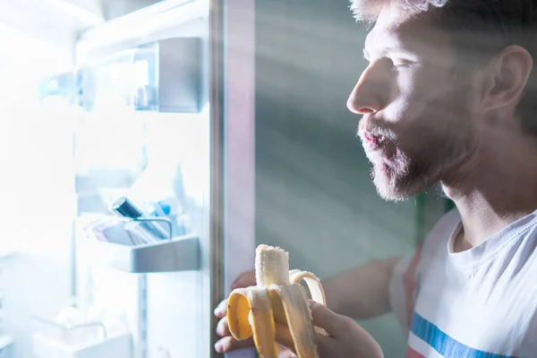 Henkilö syö terveellistä ruokaa hedelmiä jääkaapista myöhään yöllä f — kuvapankkivalokuva
