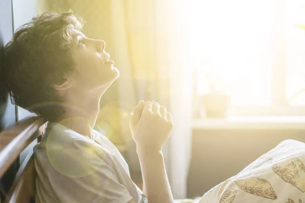 Mladý muž se modlí doma v posteli u okna b — Stock fotografie