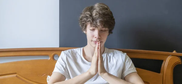 Jovem está orando na cama em casa contra a janela b — Fotografia de Stock