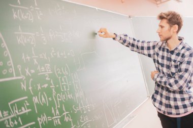 Kişi eline tebeşir alır ve B tahtasına matematiksel hesaplamalar yazar
