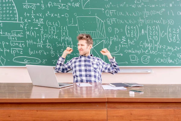 Young happy scientist sitting in front of blackboard b — Stock Photo, Image