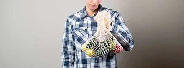A the young male hipster against the color wall carry the eco bag with fresh fruits,cotton textile eco bag — Stock Fotó