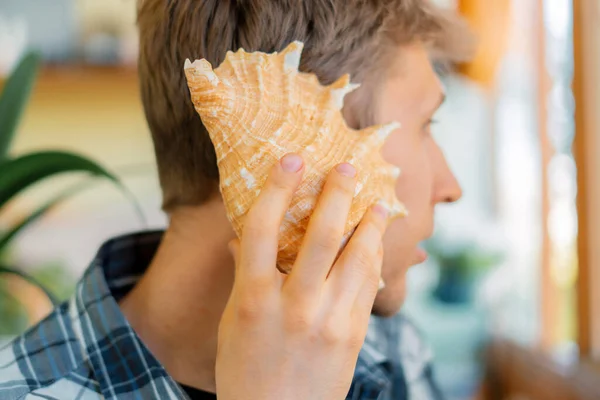 Man person som håller ett havsskal till höra, drömma och höra ljudet — Stockfoto