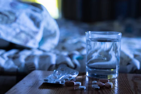 Alcune pillole medicinali e un bicchiere d'acqua sul comodino accanto al letto di notte, concetto di insonnia trattamento — Foto Stock