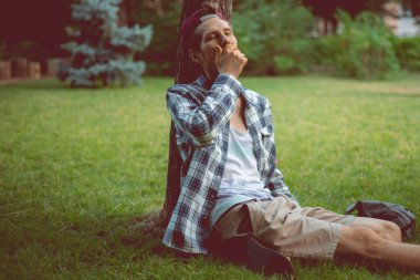 Genç erkek, halk parkında, ağacın altındaki çimlerin üzerinde uyuyor.