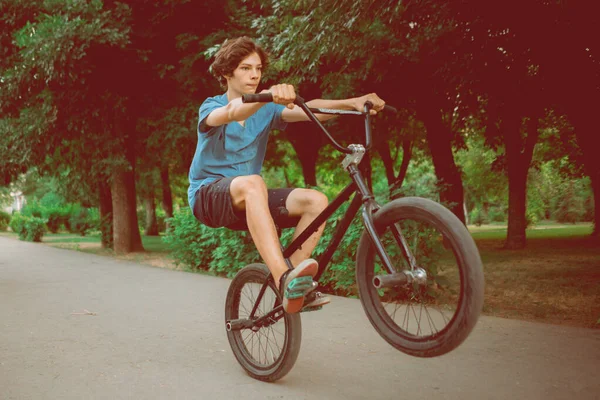 Młody człowiek jadący na rowerze bmx na tylnym kole, robiący sztuczki w mieście — Zdjęcie stockowe