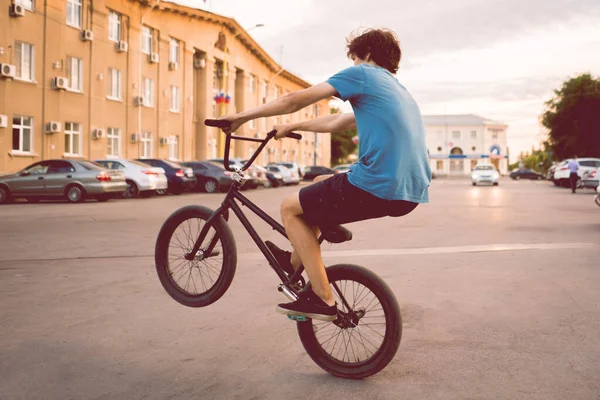 Młody człowiek jadący na rowerze bmx na tylnym kole, robiący sztuczki w mieście — Zdjęcie stockowe