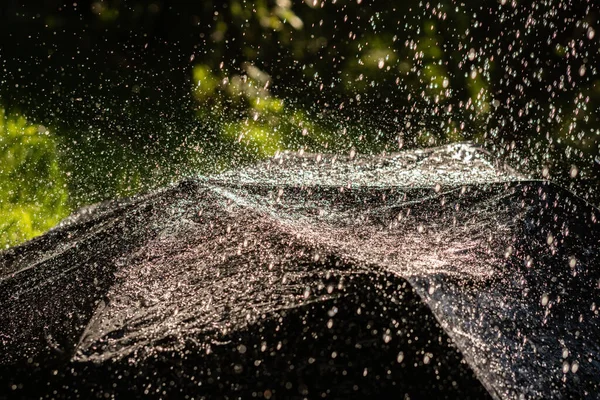 Крупним планом чорна парасолька з бризками та краплями під час сильного дощу на відкритому повітрі — стокове фото