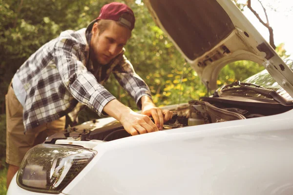 Jeune homme déçu debout à la voiture cassée avec capot ouvert pour vérifier les moteurs Image En Vente