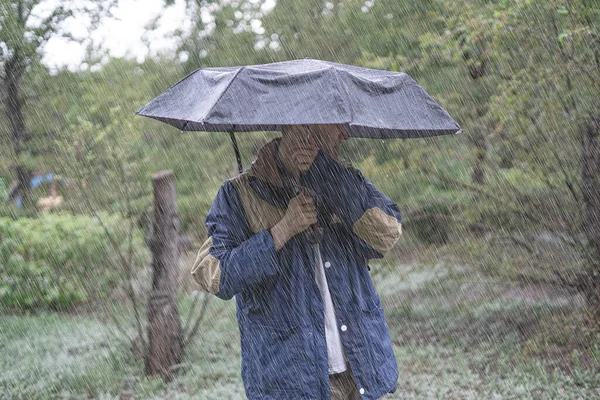 Młody człowiek stojący pod parasolem chroni przed intensywnym deszczem tropikalnym w lesie — Zdjęcie stockowe