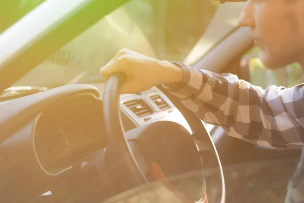 Pemuda santai dalam kemeja kotak-kotak mengendarai mobil selama matahari terbenam — Stok Foto