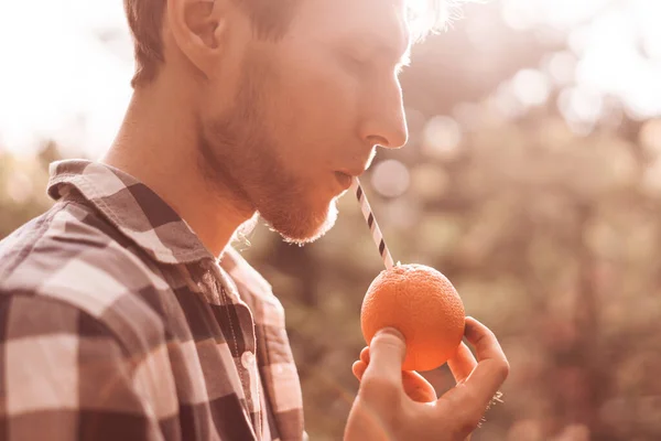 Az a fiatal, aki a narancsgyümölcsöt tartja, és a benne lévő tubulusával együtt iszik — Stock Fotó