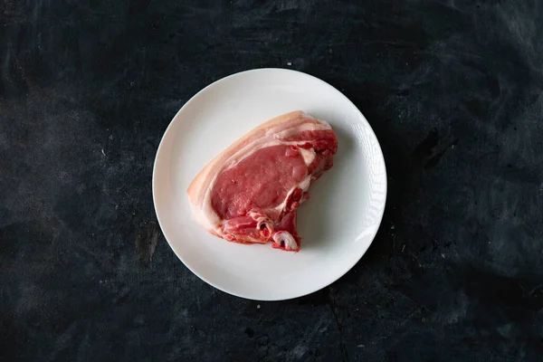 Surowy plaster wieprzowiny lub stek na białej ceramicznej płytce z dodatkiem przypraw i izolatów ziół — Zdjęcie stockowe
