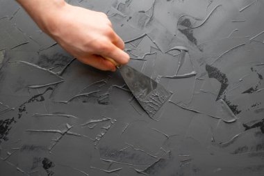 Elinizi spatula ya da macun bıçağıyla kapayın. Duvara gri macun koyun. Süsleme işlemi için.