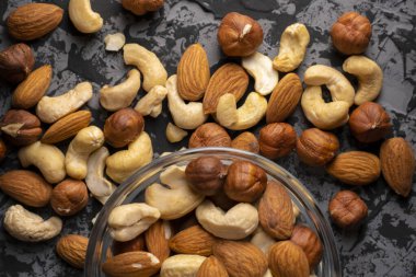 Karanlık bir masada, sağlıklı ve organik gıda kavramlarının olduğu bir kasede farklı ham kokteyl fındıkları karıştırdım.