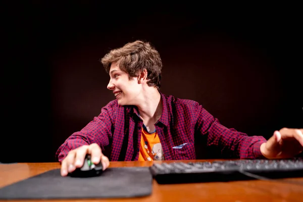 Jovem do sexo masculino jogar jogos de computador em uma mesa em um quarto escuro b — Fotografia de Stock