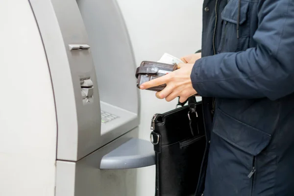 Las personas sostienen una cartera con dinero en efectivo y retiran algo de dinero en cajero automático — Foto de Stock