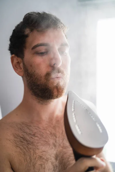 Man Blowing Hot Iron Emitting Steam While Doing Household Chores — Stock Photo, Image