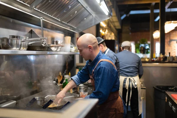 Bald Man Använder Tång För Att Blanda Pasta Stekpanna Medan — Stockfoto