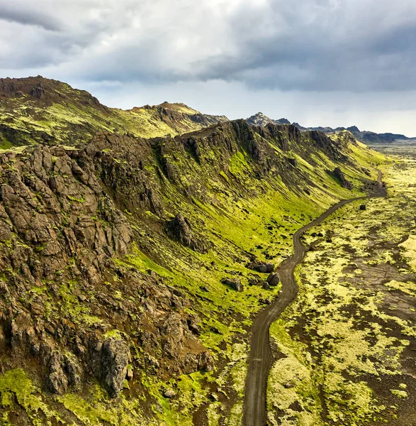 アイスランドの曇りの日に道路や乾燥した地形の近くに位置する山の空中ビュー — ストック写真