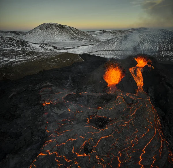 从火山口喷出并沿着岩石地面流动的炽热橙色熔岩的图片 — 图库照片
