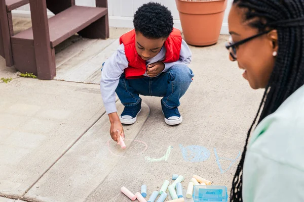 Ragazzo Che Usa Gesso Disegnare Sul Cemento Mentre Madre Sorride — Foto Stock