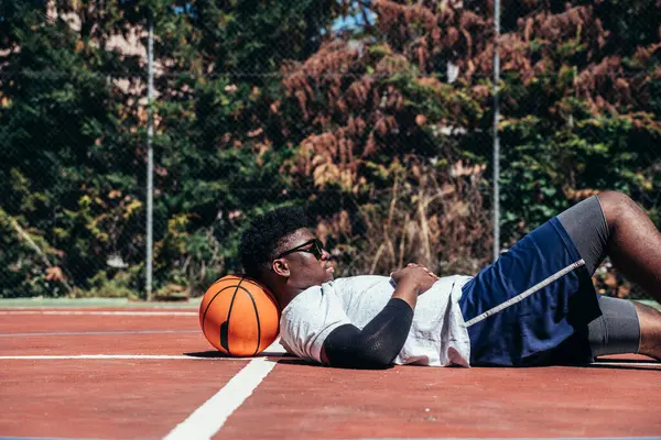 黑人小伙子在篮球场上躺着 一边用手机 技术和体育概念 — 图库照片