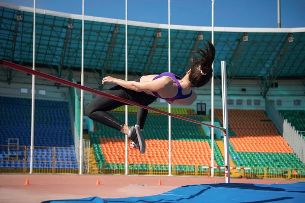 陸上競技場でトラックやフィールドワーク中にバーを飛び越える強力な女性選手 — ストック写真