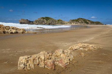 Robberg Doğa Rezervi, Plettenberg Körfezi, Güney Afrika 'daki kumlu sahil ve kayaların mavi gökyüzüne karşı manzarası