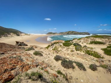 Robberg Doğa Rezervi, Plettenberg Körfezi, Güney Afrika 'daki kumlu sahil ve kayaların mavi gökyüzüne karşı manzarası