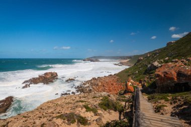 Robberg Doğa Koruma Alanı, Plettenberg Körfezi, Güney Afrika 'da mavi gökyüzüne karşı kayaların arasından geçen tahta yürüyüş patikası.