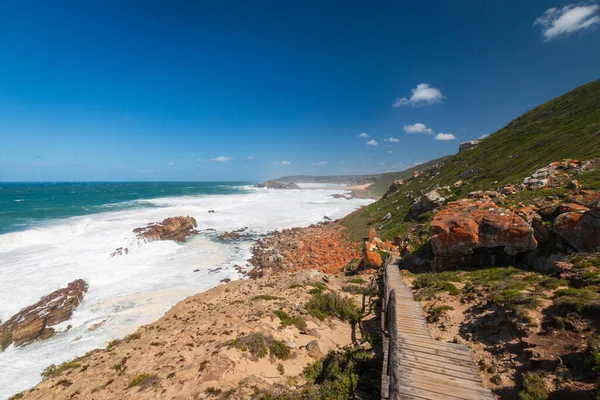 Robberg Doğa Koruma Alanı, Plettenberg Körfezi, Güney Afrika 'da mavi gökyüzüne karşı kayaların arasından geçen tahta yürüyüş patikası.
