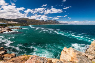 Hermanus ve Walker Körfezi 'nin manzarası Cape Town, Güney Afrika yakınlarındaki uçurum yolundan bulutlu mavi gökyüzüne karşı