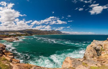 Hermanus ve Walker Körfezi 'nin manzarası Cape Town, Güney Afrika yakınlarındaki uçurum yolundan bulutlu mavi gökyüzüne karşı
