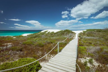 Fynbos bitki örtüsünden geçerek Hindistan Okyanusu kıyısındaki De Hoop doğa koruma alanındaki güzel kum tepelerine uzanan tahta patika yolu manzarası. Güney Afrika gökyüzüne karşı.