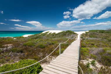 Fynbos bitki örtüsünden geçerek Hindistan Okyanusu kıyısındaki De Hoop doğa koruma alanındaki güzel kum tepelerine uzanan tahta patika yolu manzarası. Güney Afrika gökyüzüne karşı.