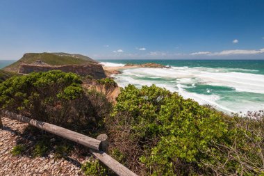 Hint Okyanusu manzarası ve kıyı şeridi Robberg Doğa Rezervi 'nde ahşap patika, Plettenberg Körfezi, Güney Afrika mavi gökyüzüne karşı