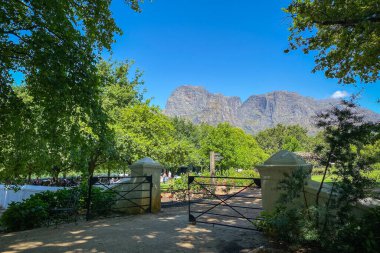Solunda piknik bahçesi olan Güney Afrika 'daki Boschendal Şaraphanesi' nde Rhone Homestead 'de demir kapı ve mavi gökyüzüne karşı Hottentots Holland Dağları.