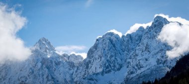 Karla kaplı Prik (solda) ve Razor (sağda) dağları, Slovenya 'nın Kranjska Gora üzerinde bulutlu mavi gökyüzüne karşı yükseliyor