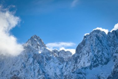 Karla kaplı Prik (solda) ve Razor (sağda) dağları, Slovenya 'nın Kranjska Gora üzerinde bulutlu mavi gökyüzüne karşı yükseliyor