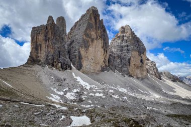 İtalya 'daki Tre Cime di Lavaredo' nun yakın görüntüsü, soluk kireç taşı parkeleri üzerinde yükselen üç Dolomite kulesi ve mavi gökyüzüne karşı mavi bulutlar.