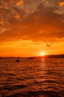 İstanbul, Türkiye 'nin Avrupa yakasındaki Beyoğlu ve Eminonu' ya bakan, çarpıcı yanan gökyüzü, parıldayan su ve tekneler ile Boğaz 'ın üzerinde güzel altın bir gün batımı.