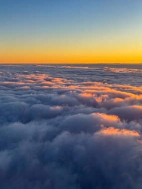 Altın şafak ışığı bulutların dalgalanan denizi üzerinde yıkanır. Açık ufuk altında; Pastel gökyüzü ve yumuşak parıltı bulutların üzerinden sakin bir gündoğumu sahnesi oluşturur.