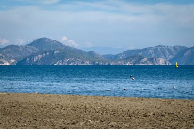 Dalaman yakınlarındaki Sarigerme 'de kumlu bir sahil. Türkiye' nin Ege sahilinde, açık mavi gökyüzü altında dalgalar ve uzak dağlarla..