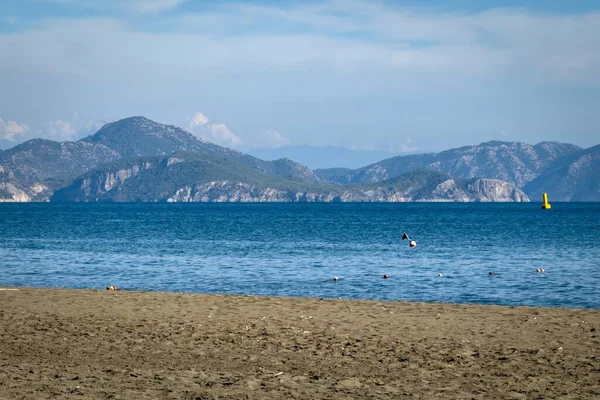 Dalaman yakınlarındaki Sarigerme 'de kumlu bir sahil. Türkiye' nin Ege sahilinde, açık mavi gökyüzü altında dalgalar ve uzak dağlarla..